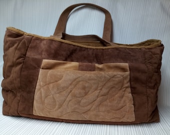 May include: A brown quilted tote bag with a large pocket on the front. The bag has a brown leather handle and is made of a soft, suede-like material.