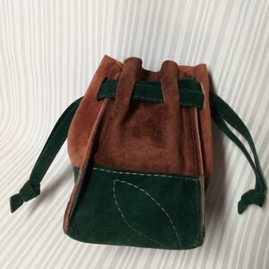 May include: A brown and green suede drawstring bag with a leaf design. The bag has a brown top and a green bottom.