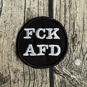 Könnte beinhalten: Ein runder, schwarzer Aufnäher mit weiß gesticktem Text. Der Text lautet "FCK AFD". Der Aufnäher ist wahrscheinlich zum Aufnähen oder Aufbügeln auf Kleidung oder Accessoires gedacht.