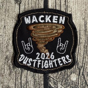 Könnte beinhalten: Ein schwarzer gestickter Aufnäher mit dem weißen Schriftzug WACKEN oben und DUSTFIGHTERS unten. In der Mitte befindet sich eine braune Tornado-Grafik, flankiert von zwei weißen Hand-Symbolen, die das Rock-Zeichen zeigen, sowie der Jahreszahl 2026.