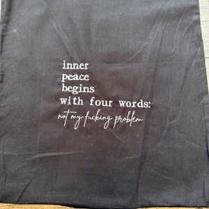 Puede incluir: Bolsa negra con cord&oacute;n y texto blanco: "la paz interior comienza con cuatro palabras: no es mi puto problema."