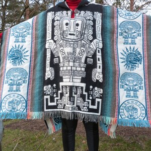 May include: A black, white, and blue poncho with a geometric pattern and fringe. The poncho features a large, stylized figure in the center.