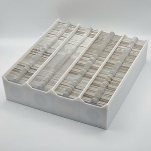 Puede incluir: Una caja de almacenamiento de plástico blanca con múltiples compartimentos llenos de pequeños objetos redondos blancos.