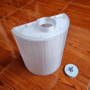 Könnte beinhalten: Ein weißer Plastikbehälter mit einer strukturierten Oberfläche und einer runden Öffnung oben. Der Behälter steht auf einer Holzoberfläche. Ein kleiner, grauer Plastikdeckel mit einem sternförmigen Design liegt neben dem Behälter.
