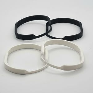 Peut inclure: Quatre anneaux en plastique, deux noirs et deux blancs, sont disposés en un tas lâche. Les anneaux sont tous de la même taille et de la même forme, et ils semblent être faits d'un matériau flexible.