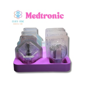 May include: A purple plastic organizer holds several sealed medical devices. The devices are packaged in clear plastic and feature the brand name "Medtronic" in pink text. The logo for "Gluco Hive Diabetes Care" is in the upper left corner.