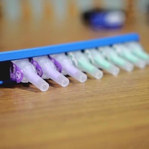 May include: A blue plastic holder with multiple clear plastic needle tips. The tips are arranged in rows and are partially visible.