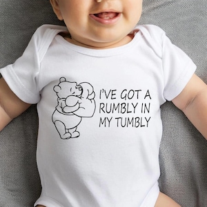 May include: White baby onesie with a black graphic of Winnie the Pooh hugging a honey pot and the text "I've got a rumbly in my tumbly". The onesie is short-sleeved and has a snap closure.
