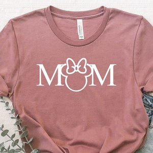 May include: A mauve t-shirt with a white graphic of the word "MOM" with a Minnie Mouse head and bow in the centre of the word.