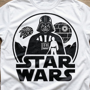 Może przedstawiać: Biała koszulka z czarno-białą grafiką Star Wars. Projekt zawiera Dartha Vadera, Sokoła Millennium, Gwiazdę Śmierci i napis "STAR WARS". Klasyczny t-shirt dla fanów.