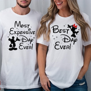 以下が含まれることがあります： 黒い文字と画像が書かれた白いTシャツ2枚。最初のTシャツには「Most Expensive Day Ever!」と書かれており、ミッキーマウスの黒いシルエットが描かれている。2枚目のTシャツには「Best Day Ever!」と書かれており、赤いリボンをつけたミニーマウスの黒いシルエットが描かれている。