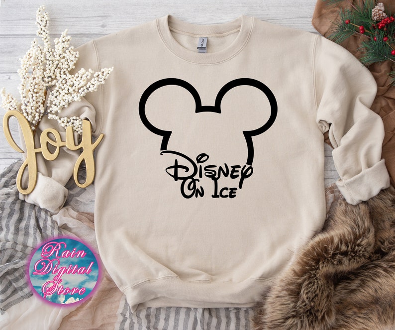 May include: A beige sweatshirt with a black Mickey Mouse head and the text "Disney On Ice" printed on the front.