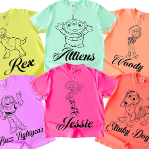Peut inclure: Plusieurs t-shirts colorés avec des motifs de personnages de dessins animés. Les chemises sont de différentes couleurs, dont le jaune, le vert, le rose et l'orange. Chaque chemise présente un design de personnage différent avec le nom du personnage en dessous.