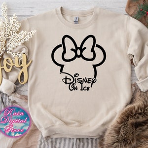 May include: A beige sweatshirt with a black outline of Mickey Mouse's head with a bow and the text "Disney On Ice" underneath.