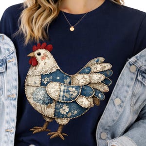 Puede incluir: Camiseta azul marino con un diseño de gallina de retazos. La gallina tiene una cresta roja, patrones florales y de cuadros en tonos azules y un cuello de encaje. La camiseta es de estilo cuello redondo clásico.