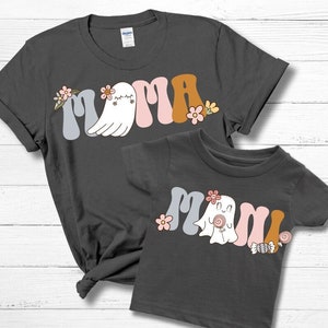 May include: Two charcoal grey t-shirts, one adult and one child size, with the word "Mama" in a retro font. The "M" and "a" are light blue, the second "a" is pink, and the ghost is white. Floral and candy accents.