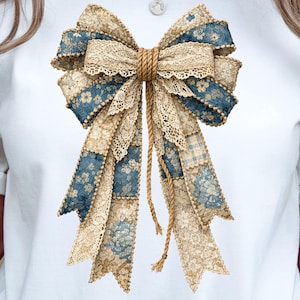 Può includere: Un grande fiocco decorativo con un design patchwork. Presenta motivi floreali blu, pizzo color crema e tessuto beige. Il fiocco è legato con una corda spessa e ha lunghi nastri fluenti. Il fiocco è centrato su uno sfondo bianco.