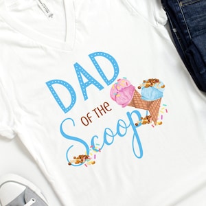May include: White v-neck t-shirt with blue text that reads "Dad of the Scoop" and two ice cream cones with pink and blue ice cream.