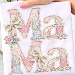 Può includere: Un tessuto bianco con la scritta "Mama" applicata in un design patchwork. Le lettere sono decorate con motivi floreali, pois rosa e quadretti blu. Ogni lettera è delineata con perle finte e ornata con fiocchi di pizzo e accenti floreali.