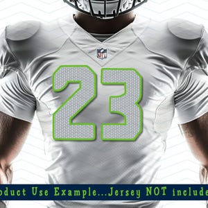 Puede incluir: Camiseta de f&uacute;tbol americano blanca con el n&uacute;mero 23 en un patr&oacute;n de punto gris con contorno verde. La camiseta tiene el logo de la NFL y hombreras. El texto en la parte inferior dice "Product Use Example...Jersey NOT included."