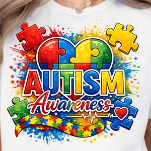 May include: White t-shirt featuring a colorful graphic design for Autism Awareness. The design includes puzzle pieces, a heart, and the words "AUTISM Awareness" in bold, vibrant colors. The shirt is a crew neck.