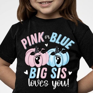 Może przedstawiać: Czarny T-shirt z napisem "Pink or Blue Big Sis loves you!" w kolorze białym i różowym. Przedstawiono dwie dynie, jedną różową i jedną niebieską, z odciskiem stopy na każdej.