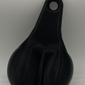 Könnte beinhalten: Ein schwarzes, 3D-gedrucktes Novelty-Item in Form eines Hodensacks, mit einer Schlaufe oben zum Aufhängen. Der Artikel besteht aus einem soliden, mattschwarzen Material und hat eine strukturierte Oberfläche.