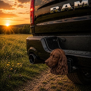 May include: A black RAM truck tailgate featuring a chrome RAM emblem and a brown, sculpted dog head hitch cover attached to the rear bumper. The hitch cover displays detailed fur texture and a realistic canine facial structure in a solid finish.