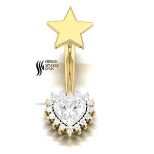 Puede incluir: Un piercing para el ombligo de color dorado con una estrella en la parte superior y una piedra preciosa en forma de corazón rodeada de piedras más pequeñas en la parte inferior. El anillo tiene un diseño curvo sobre un fondo blanco.