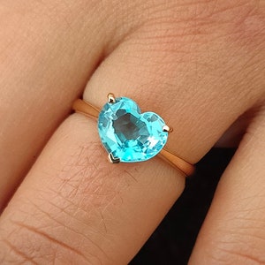 Puede incluir: Un anillo de oro con una piedra preciosa azul en forma de corazón.