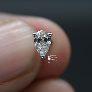 May include: A pear-shaped diamond earring with a silver setting. The diamond is clear and sparkly.