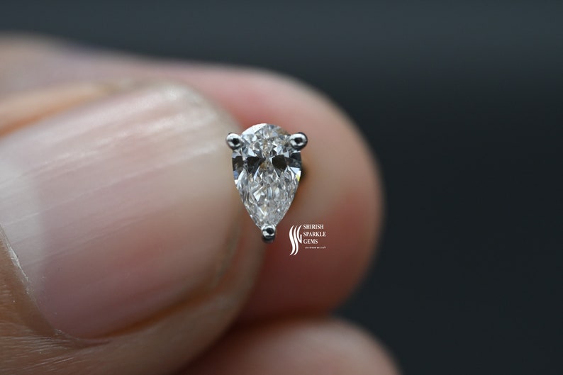 May include: A pear-shaped diamond earring with a silver setting. The diamond is clear and sparkly.