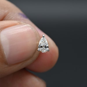 May include: A single pear-shaped diamond earring in a silver setting.