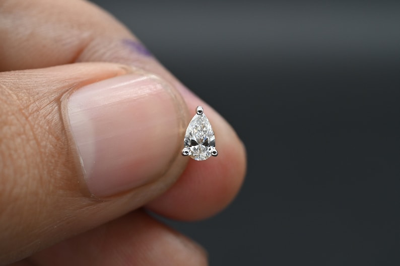 May include: A single pear-shaped diamond earring in a silver setting.