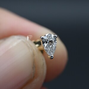 May include: A pear-shaped diamond earring set in a gold setting. The diamond is clear and sparkly.