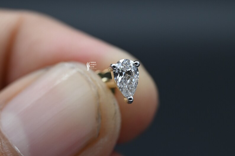 May include: A pear-shaped diamond earring set in a gold setting. The diamond is clear and sparkly.