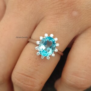 Puede incluir: Un anillo de plata con una gran piedra ovalada azul rodeada de piedras pequeñas transparentes.