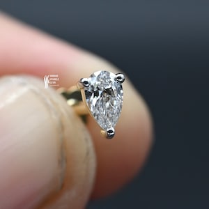 May include: A pear-shaped diamond earring with a gold setting. The diamond is clear and sparkly.