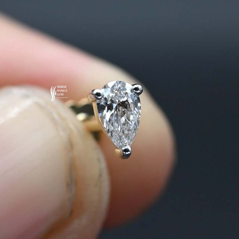May include: A pear-shaped diamond earring with a gold setting. The diamond is clear and sparkly.