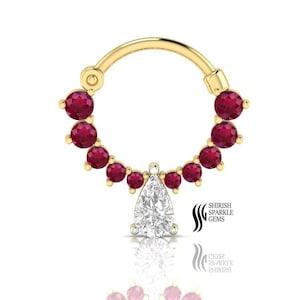 May include: Gold nose ring with a pear-shaped clear stone and a circle of red stones around it.  The ring is made of gold and has a shiny finish.  The stones are set in a prong setting.  The ring is a popular choice for nose piercings.  Shirish Sparkle Gems.