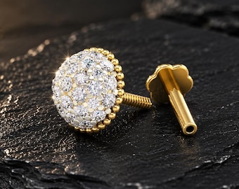 May include: A gold stud earring featuring a circular dome head encrusted with multiple clear, sparkling round-cut stones. The edge of the dome is detailed with a beaded texture. A threaded post extends from the back, ending in a flower-shaped backing.