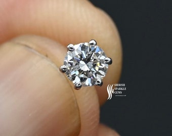 May include: A round, clear diamond gemstone set in a silver prong setting. The diamond is held in a hand.