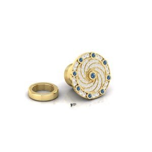 May include: A gold-colored, spiral-designed jewelry piece with a matching ring. The spiral is encrusted with small, clear stones and surrounded by blue gemstones. The jewelry is set against a white background.