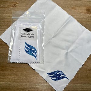 May include: White cloth with a blue glitter design and the text "Fish Extender". The design is a stylized wave with a Mickey Mouse silhouette. The cloth is packaged in a clear plastic bag.