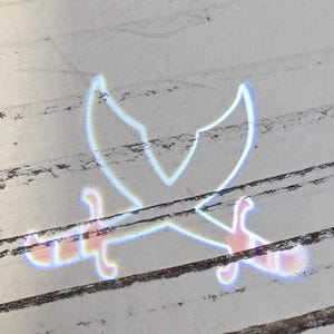 May include: An image of a crossed swords design, with a stylized, glowing effect. The swords are pale blue and pink, with a white outline, set against a white and brown wooden background.