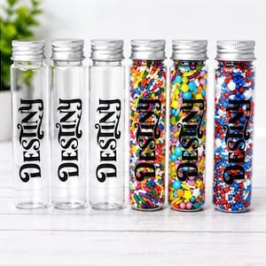 May include: Five clear glass bottles with silver lids, each labeled "Destiny" in black script. Two bottles are empty, while the others are filled with colorful sprinkles. The sprinkles include red, white, blue, yellow, and green.