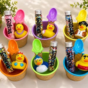 May include: Six ice cream cone-shaped bowls, each containing a clear tube filled with colorful sprinkles labeled "DESTINY," a plastic spoon, and a small rubber duck. The ducks feature various accessories including a pirate hat, sunglasses, and a shark suit.