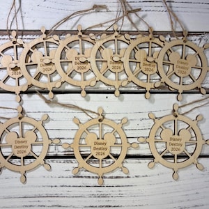 May include: Nine light-colored wooden ornaments shaped like ship wheels, each featuring a central Mickey Mouse head silhouette and the engraved text "Disney Destiny 2026". Each ornament includes a thin brown twine loop for hanging purposes.