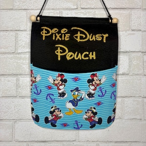 May include: A hanging fabric pouch featuring a black top section with the gold glitter text Pixie Dust Pouch and a light blue bottom section patterned with cartoon characters including Donald Duck and Mickey Mouse in nautical outfits.