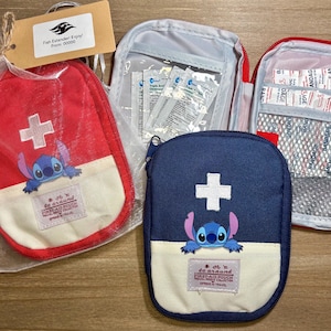 May include: A collection of first aid pouches in red, navy blue, and gray. Each pouch features a white cross and a cartoon character. One pouch is in a clear plastic bag with a tag. The pouches are on a wooden surface.
